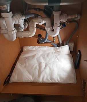 Spaghetti junction of plumbing under a kitchen sink protected by FloodSax